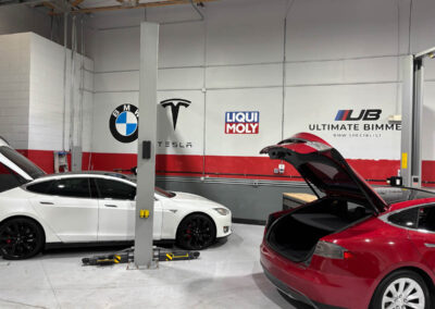 Car workshop with Tesla and BMW logos, featuring red and white cars, designed by Arizona Custom Signworks in Phoenix.