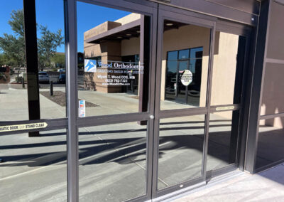 Glass entrance door of Wood Orthodontics in Phoenix, featuring Arizona Custom Signworks signage and caution notice.