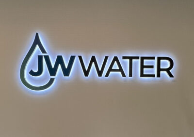Illuminated JW Water logo on wall. Designed by Arizona Custom Signworks, Phoenix. Liquid drop shape highlights sleek signage aesthetic.