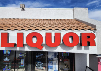 Red LIQUOR sign on a white storefront with tiled roof by Arizona Custom Signworks, Phoenix. Blue sky backdrop.